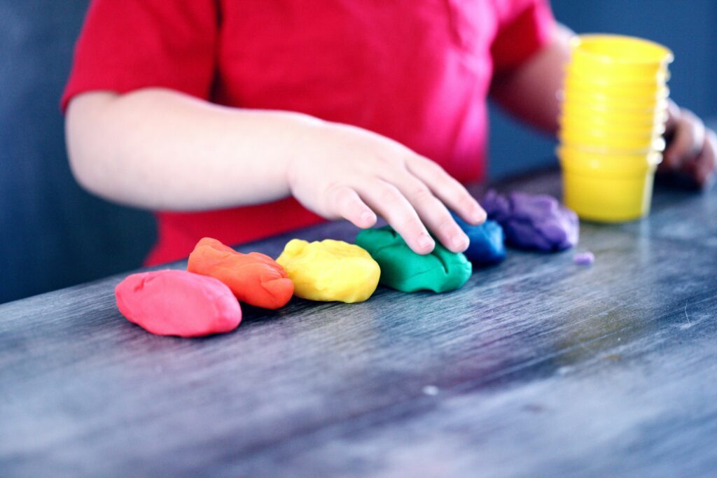 pexels photo 1449934 1449934 A young child with rainbow-colored modeling clay and stacking cups on a table indoors.